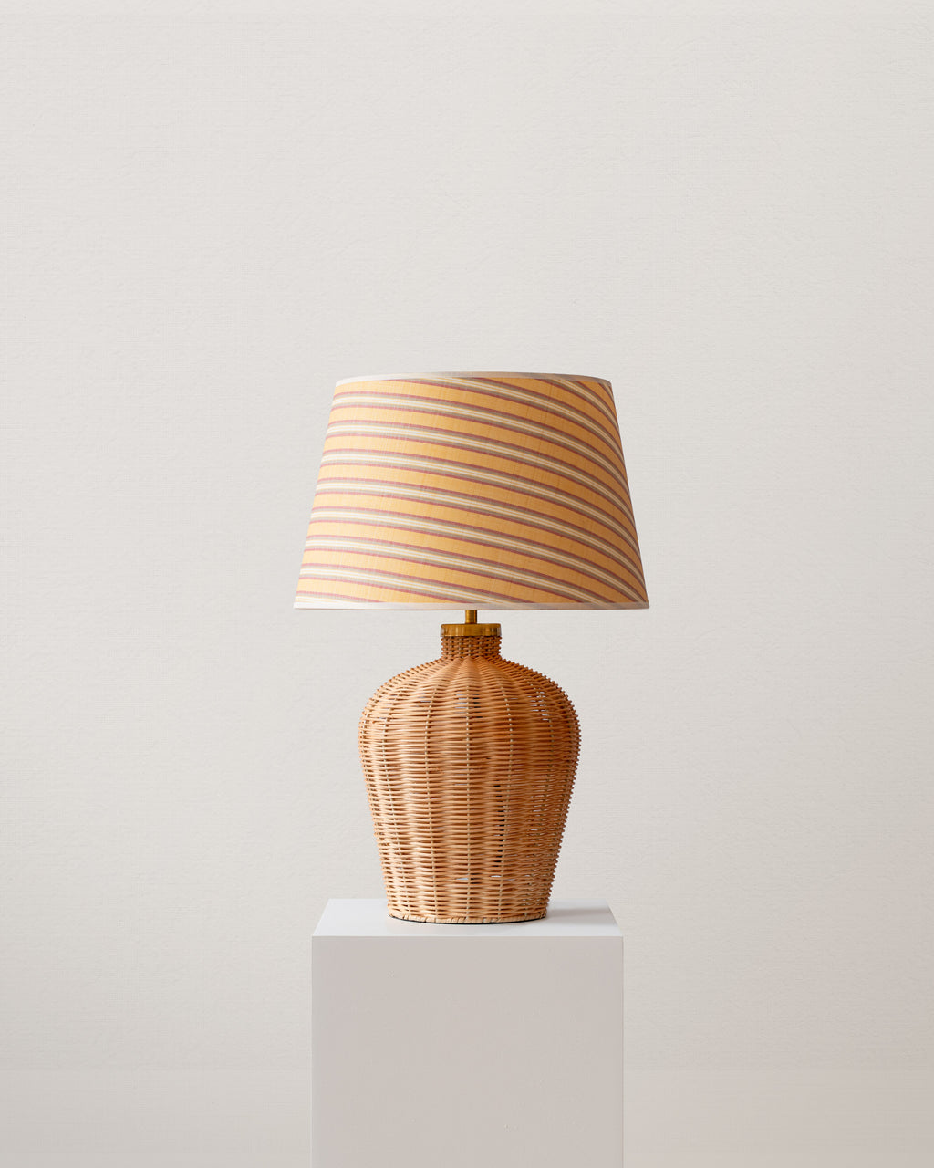 Wicker table lamp with striped shade on a white pedestal against a light gray background