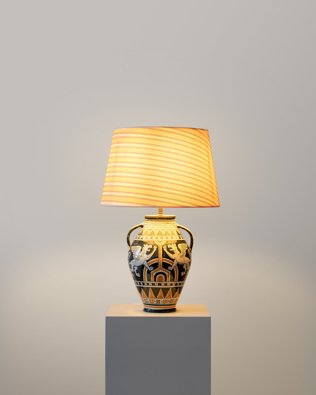 Decorative table lamp with a patterned base with a striped lampshade on a gray pedestal against a gray background