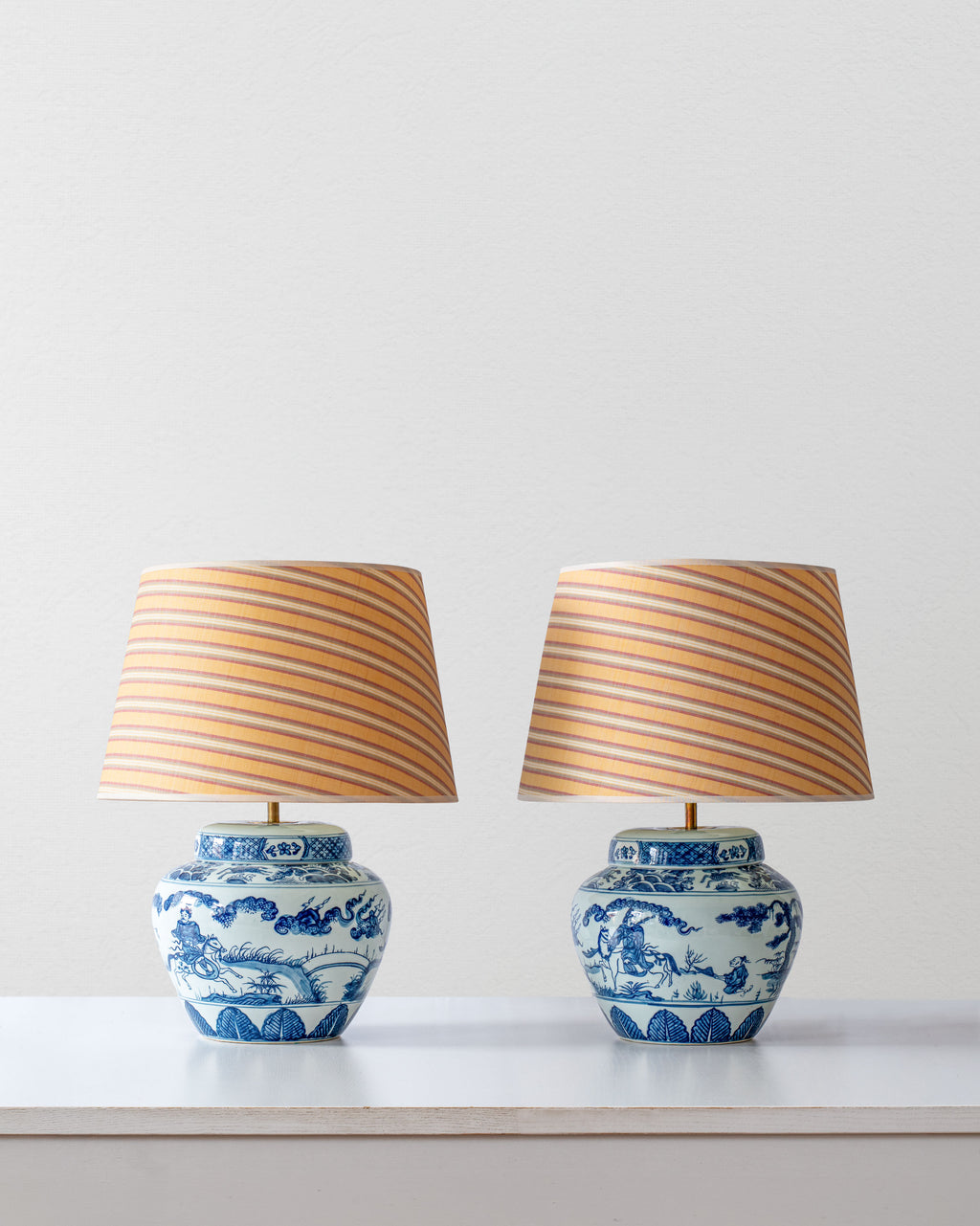 Two blue and white ceramic lamps with striped yellow shades on a white surface