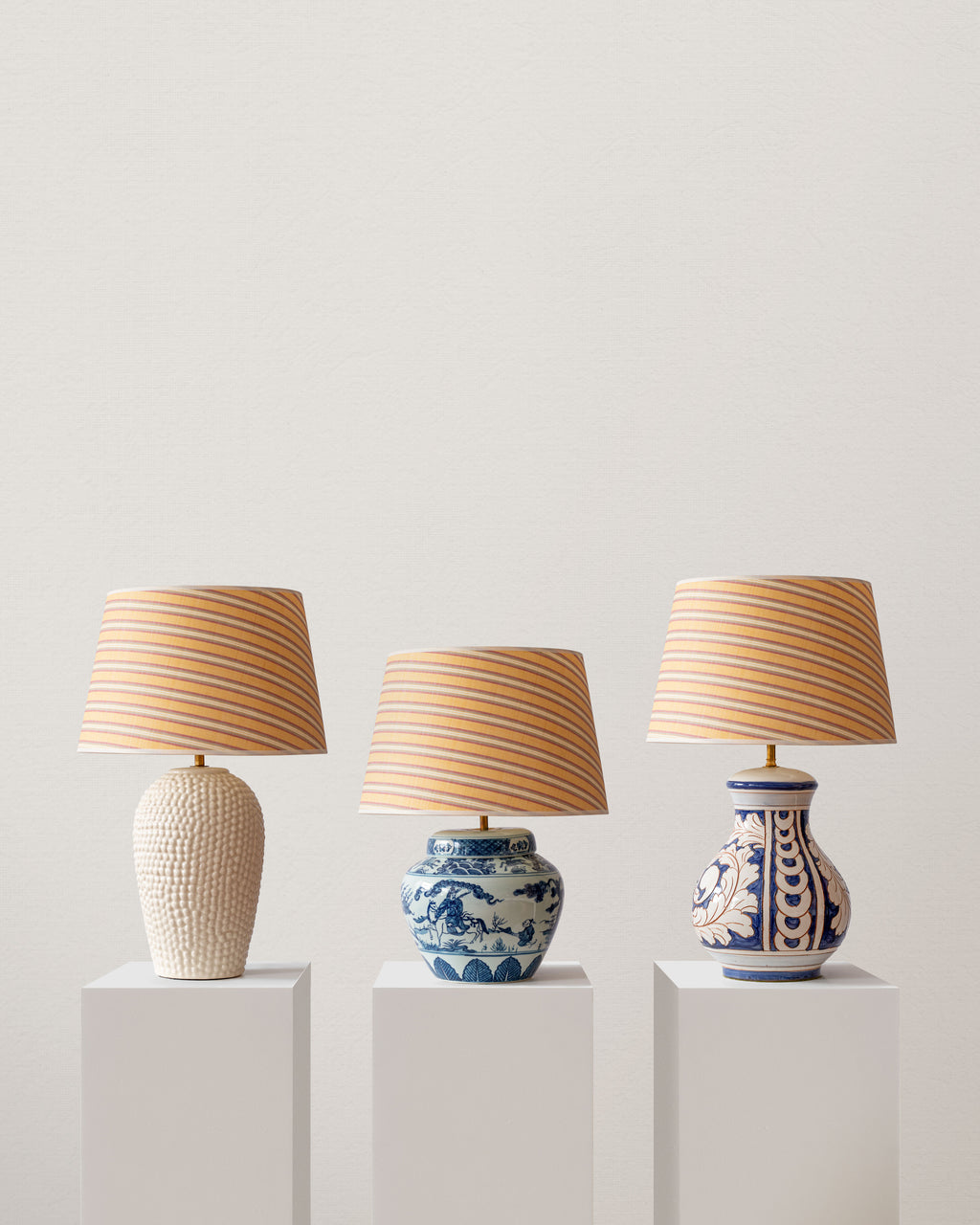 Three decorative table lamps with striped shades on white pedestals against a light gray background