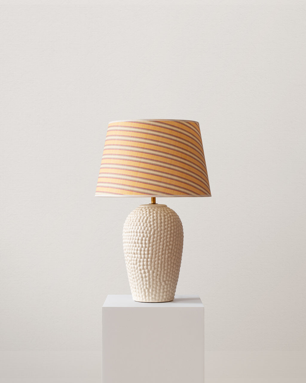Table lamp with a textured base and striped shade on a light gray pedestal against a light gray background