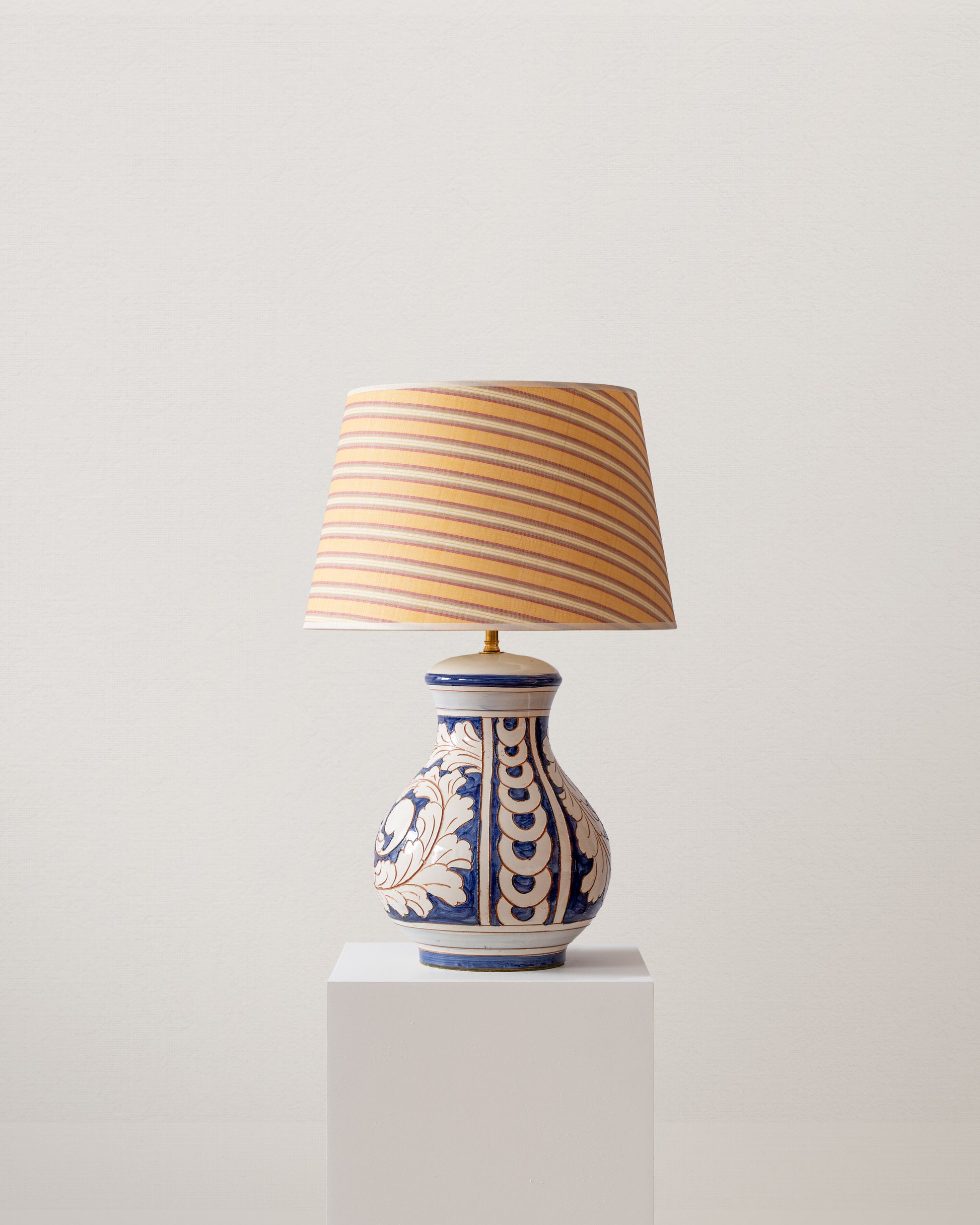 Decorative table lamp with striped shade on a white pedestal against a light gray background