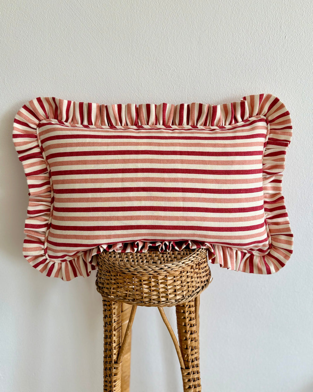 Striped pillow with ruffled edges on a wicker stool against a white wall