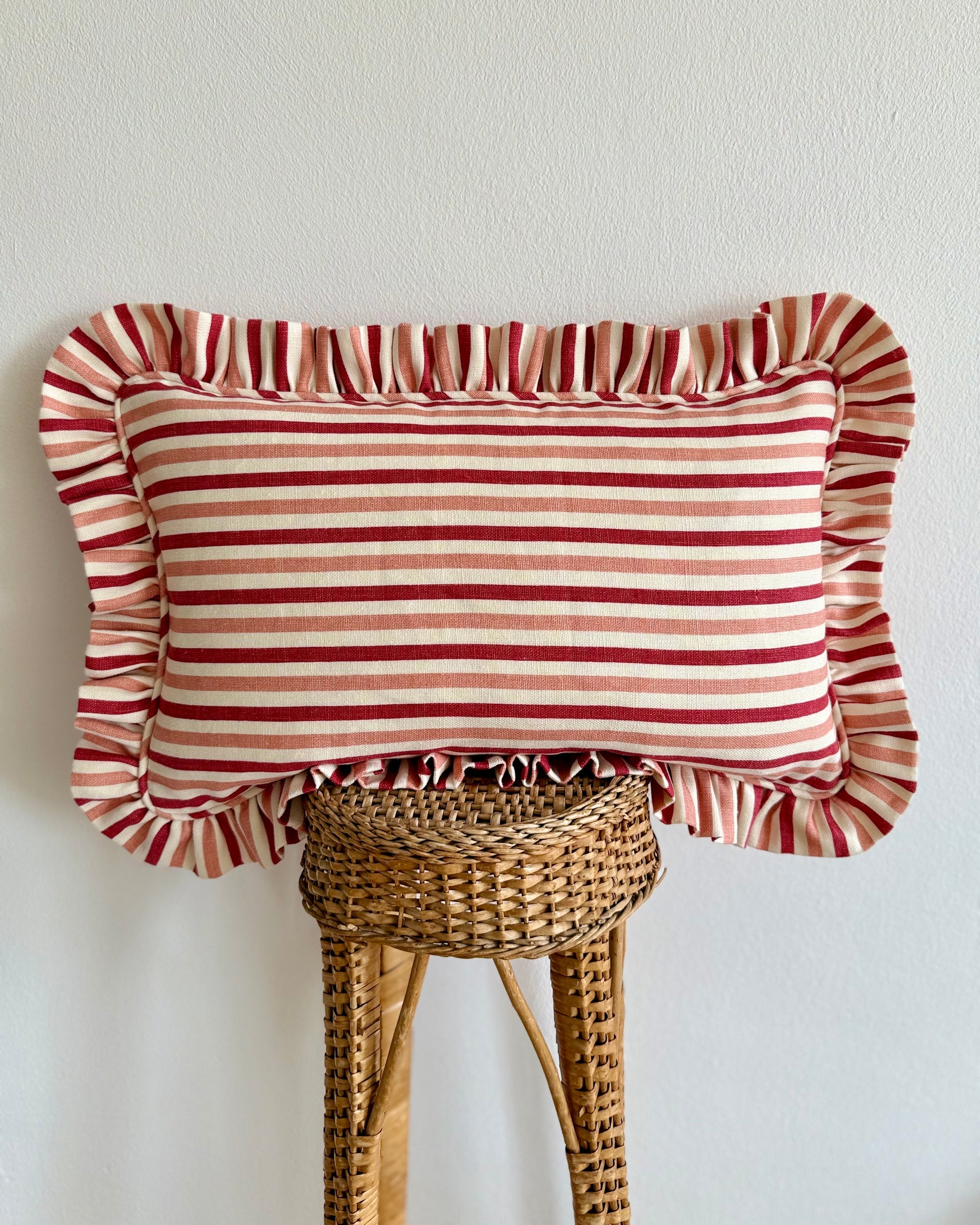 Striped pillow with ruffled edges on a wicker stool against a white wall