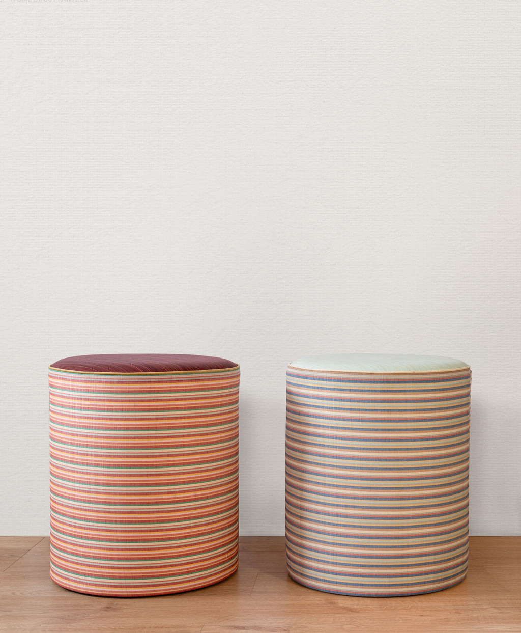 Two striped cylindrical stools on a wooden surface with a plain background