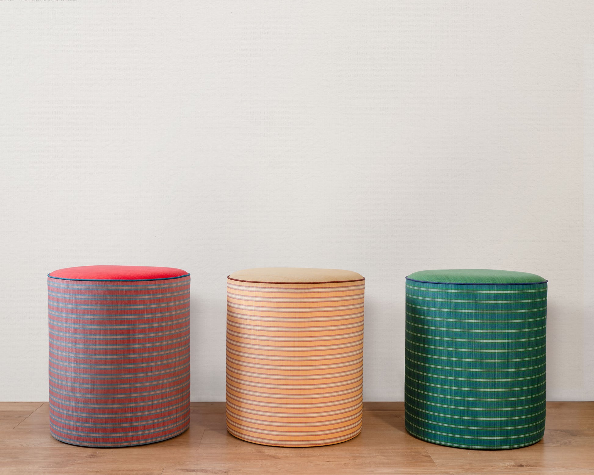 Three cylindrical stools with striped patterns on a wooden surface and light gray background