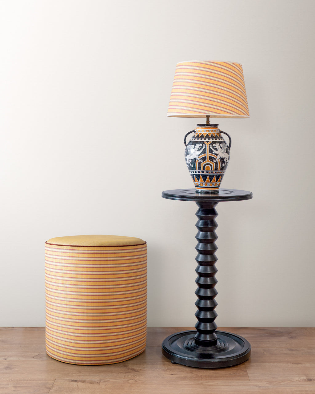 Decorative lamp with striped shade on a black pedestal table next to a striped cylindrical stool