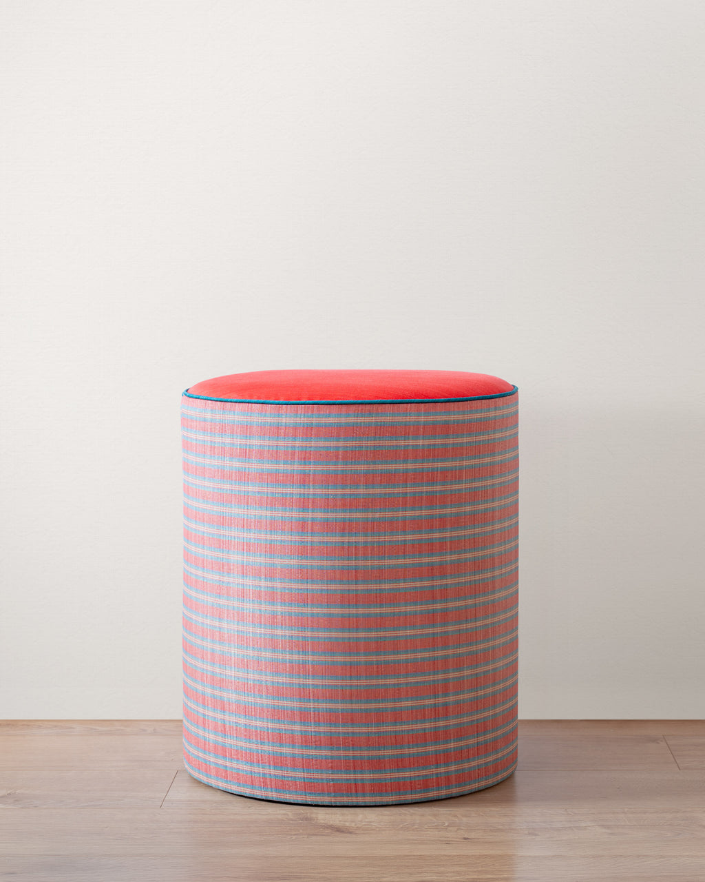 Cylindrical stool with a red top a striped red and blue pattern on a white background