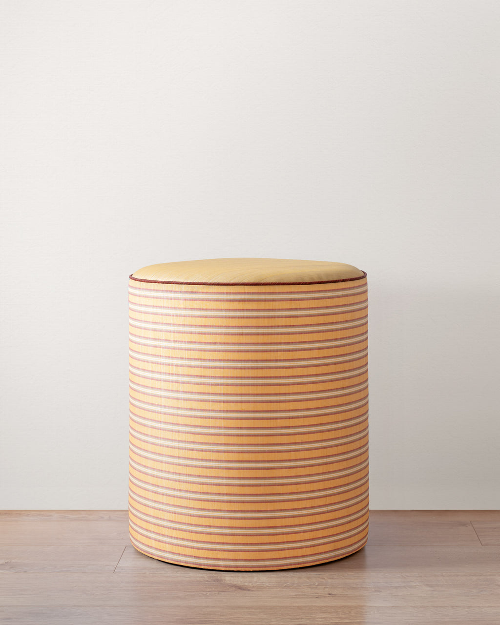 Round stool with striped pattern on a light wooden floor and white wall background