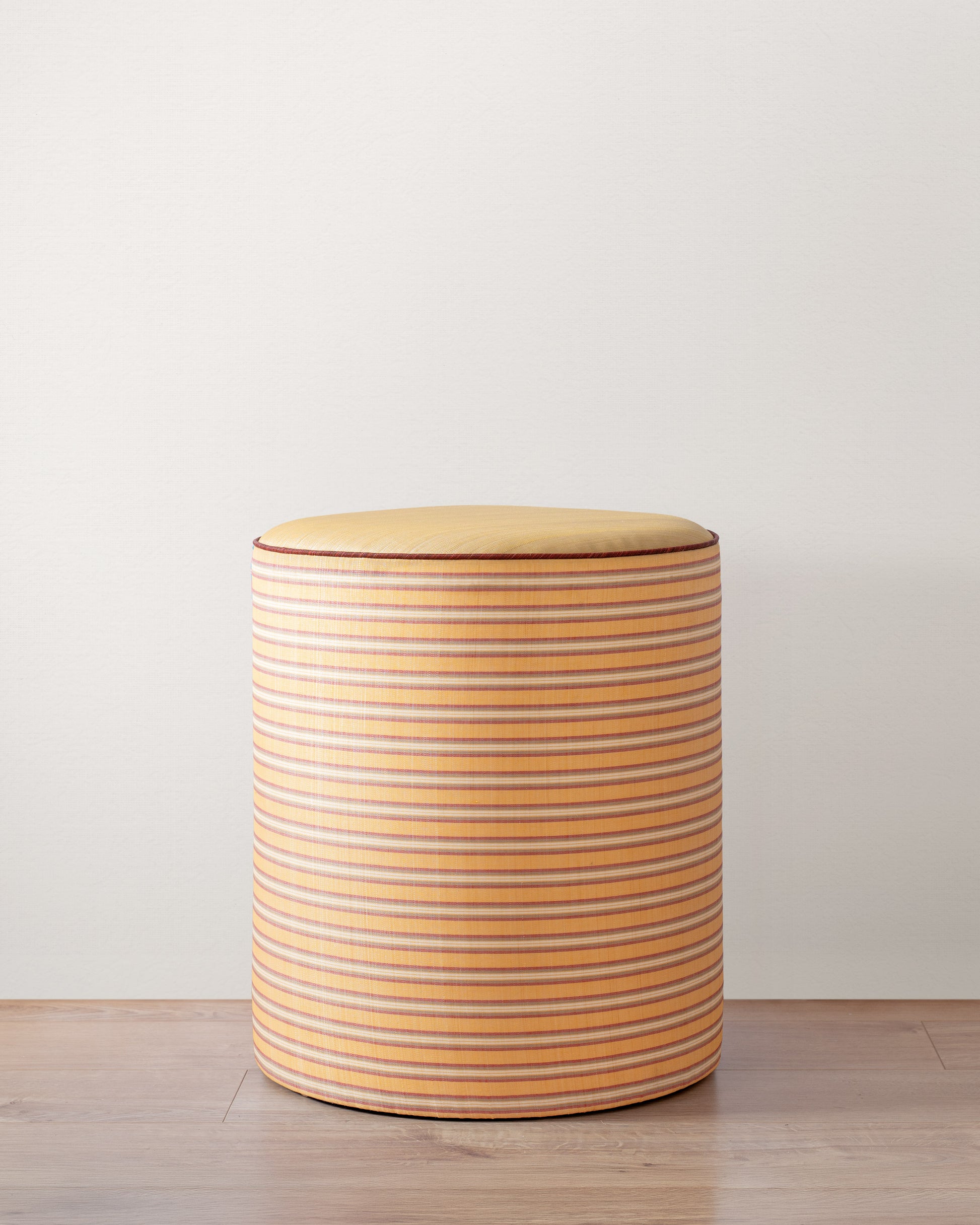 Round stool with striped pattern on a light wooden floor and white wall background